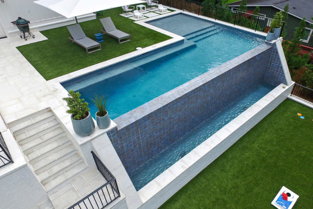 photo of a bird's eye view of a backyard pool design with a waterfall edge feature in PebbleTec Tahoe Blue Pool Finish medium blue water color
