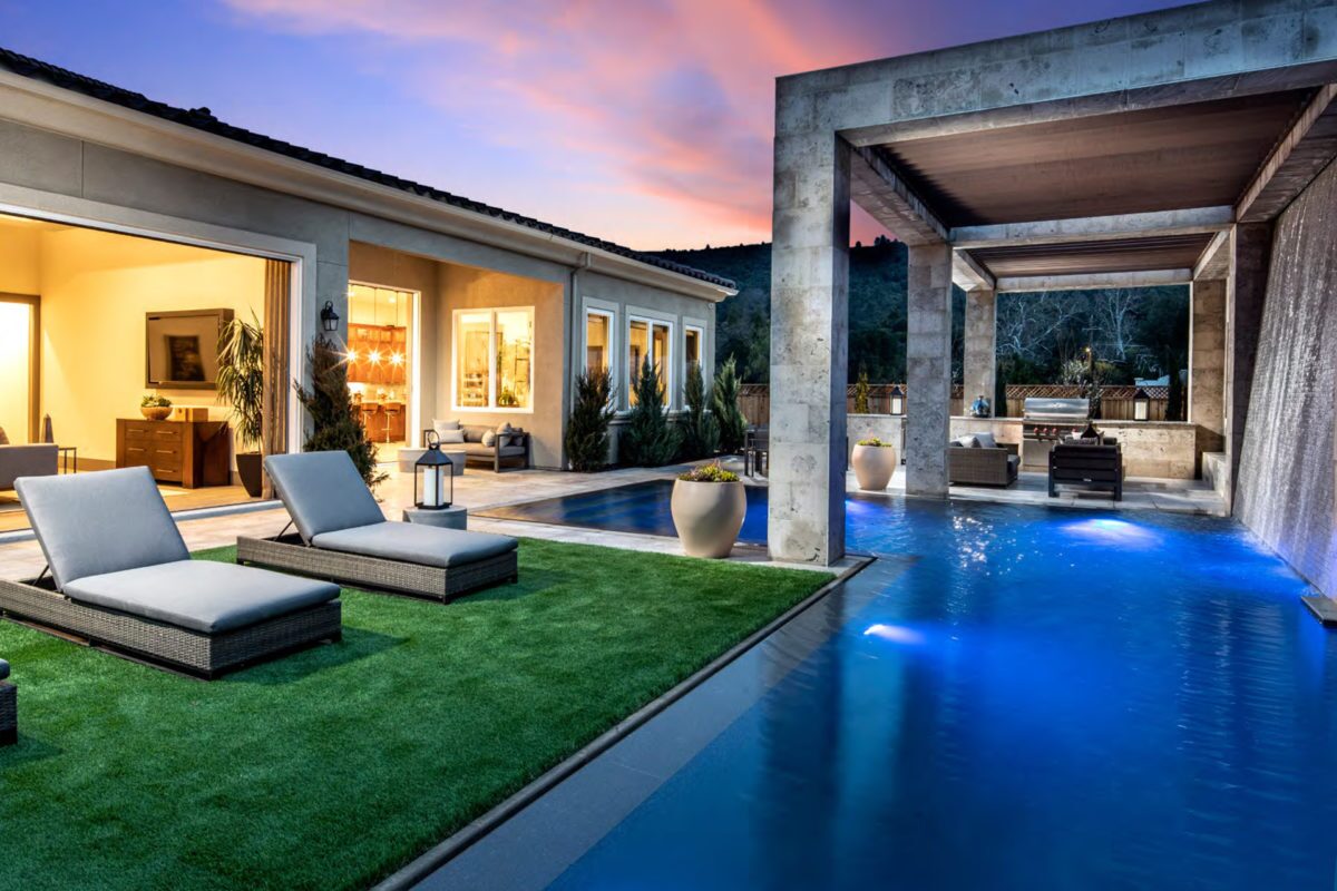 photo of a backyard pool design in the evening with a waterfall feature in PebbleTec Tahoe Blue Pool Finish medium blue water color