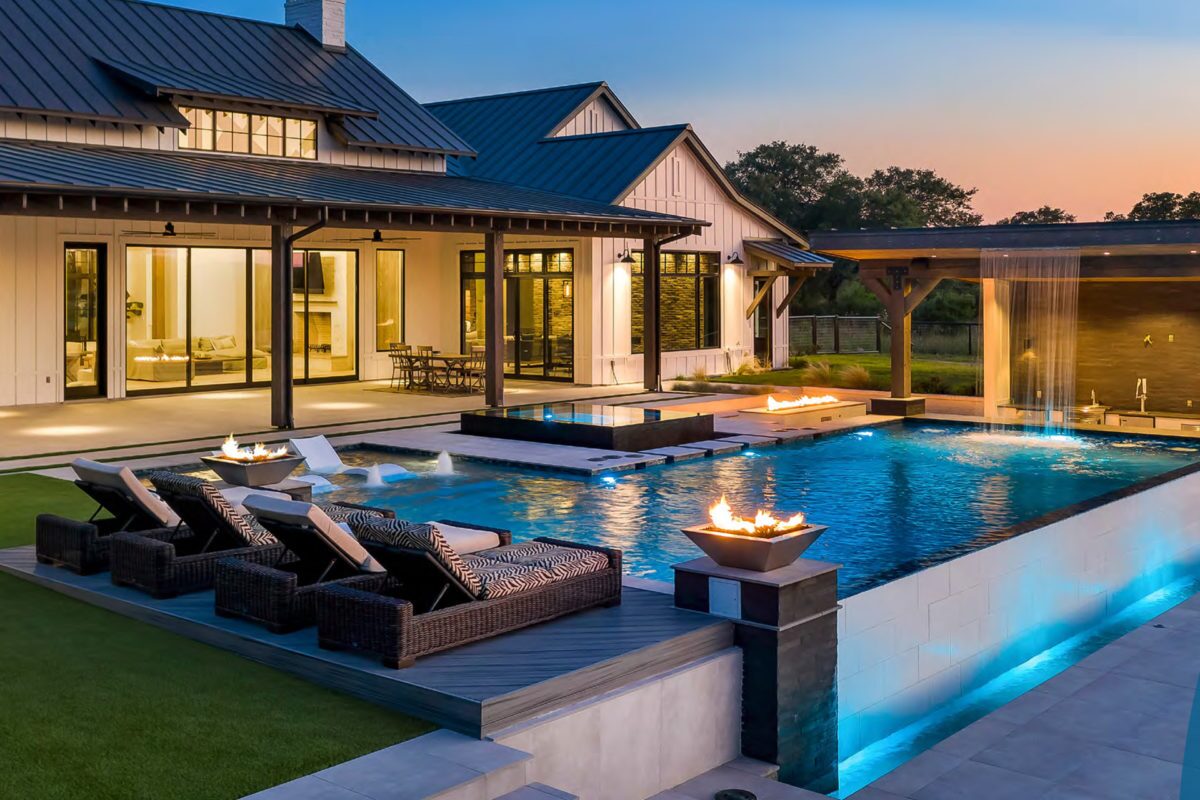 photo of a backyard pool design in the evening with a waterfall feature in PebbleTec Tahoe Blue Pool Finish medium blue water color