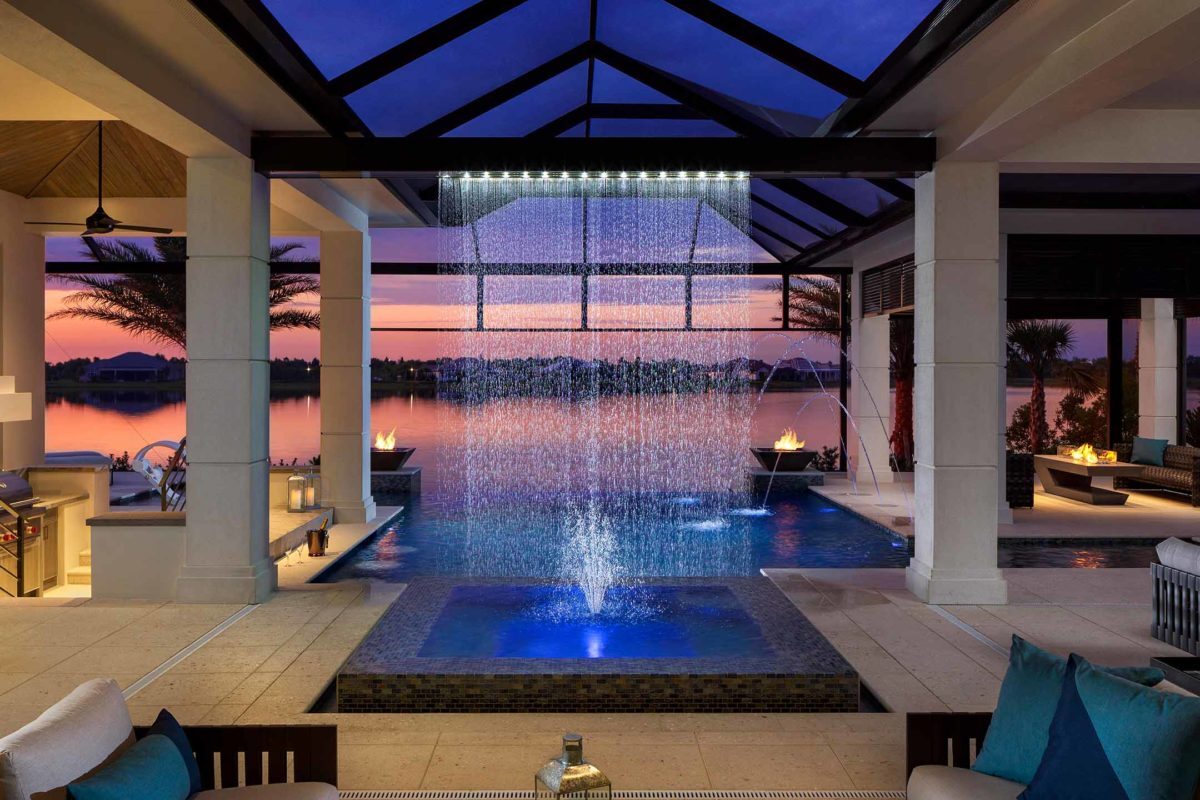 photo of a backyard pool design with waterfall water feature in PebbleTec Caribbean Blue Pool Finish by Gaetano with a sunset view over the water
