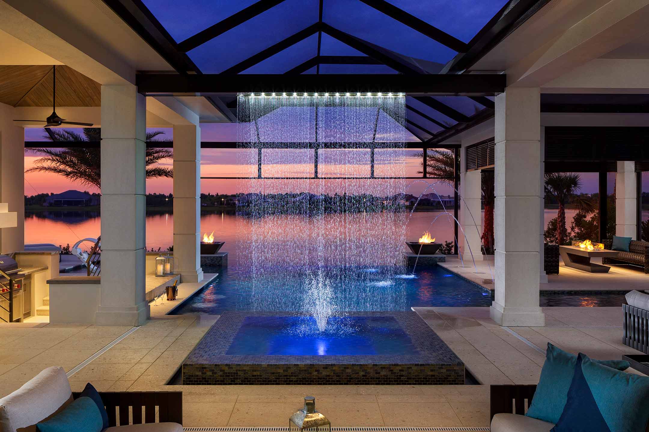 photo of a backyard pool design with waterfall water feature in PebbleTec Caribbean Blue Pool Finish by Gaetano with a sunset view over the water