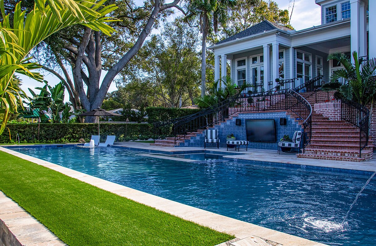 photo of a long backyard pool design in PebbleTec Blue Wave Pool Finish medium blue water color with water features